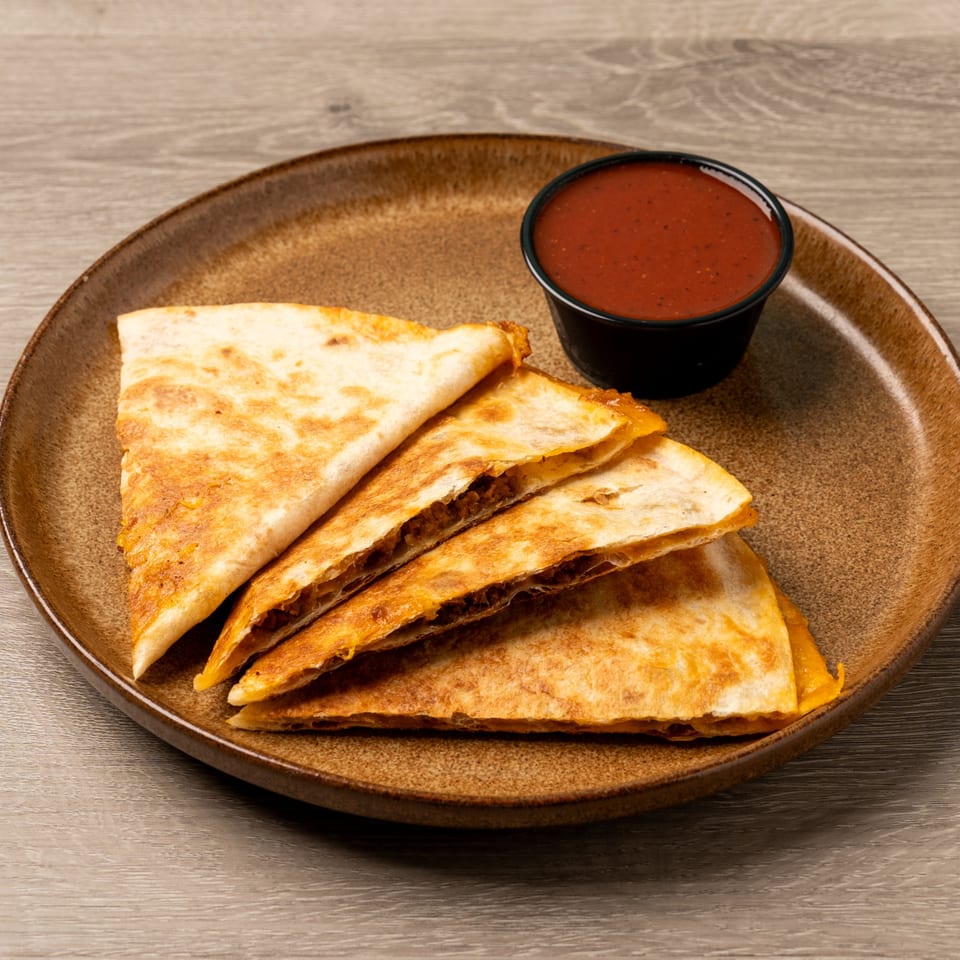 Four golden-brown quesadilla wedges filled with meat and cheese, served with a side of red salsa.