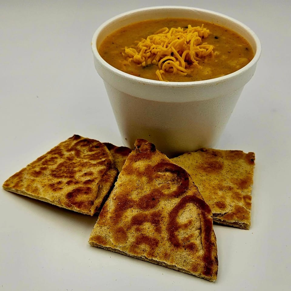 A cup of Island Taco Shack's cheesy tortilla soup with three tortilla triangles on a white surface.