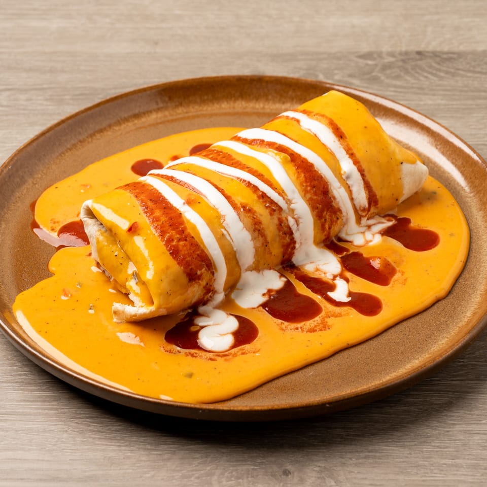A large, smothered burrito from Island Taco Shack, covered in orange sauce, sour cream, and red chili.