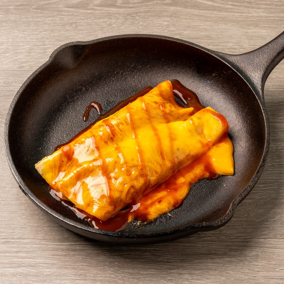 A cheesy enchilada with red sauce in a black cast iron skillet on a wooden table.