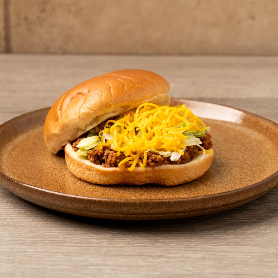 A Mexican sloppy joe with ground beef, shredded lettuce, and cheddar cheese on a bun.